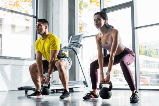 Sportsman and sportswoman doing squat with weights in sports center