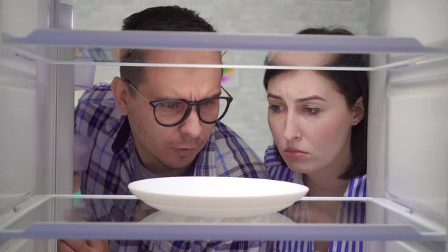 surprised and upset a married couple looks into an empty refrigerator