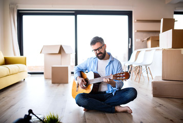 Mature man with boxes moving in new house, playing guitar.