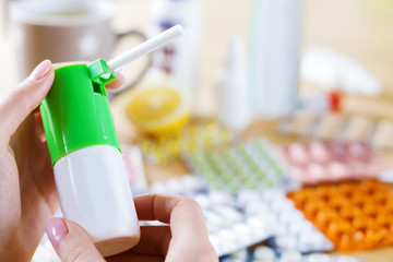 Closeup female hands are holding throat spray. Cup of tea, lemon, analgesic, antipyretic pills,...