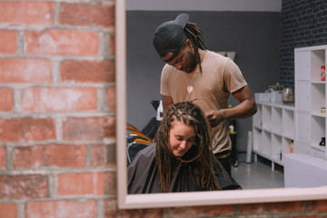 African master hairdresser  making dreadlocks for young woman in hair salon