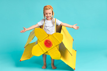 Sweet kid boy imagine flight on sky on toy airplane, yellow carboard plane. Isolated blue background