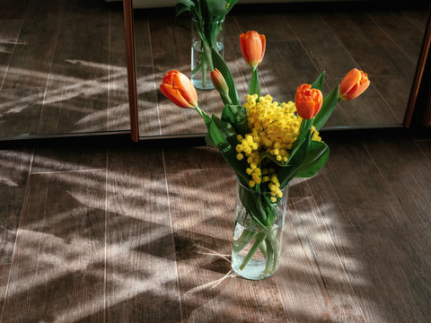 Bouquet of orange tulips and yellow mimosa on wooden floor against a mirror