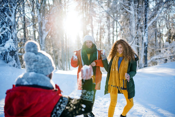 Group of young friends on a walk outdoors in snow in winter forest, having fun.