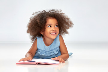 childhood, school and education concept - happy smiling little african american girl reading book...