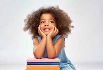 childhood, school and education concept - happy smiling little african american girl with pile of books over grey background
