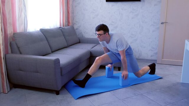 Crazy nerd man in glasses is trying to do the splits the first time on the mat at home. Sport humor concept.