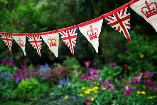 Banner of British Union Jack flag and royal crown celebratory bunting hanging in front of a flowery English summer garden background
