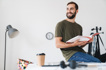 Image of caucasian smiling man holding brochure while sitting on desk