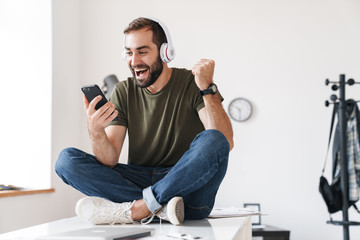 Image of young man listening music with headphones and using cellphone