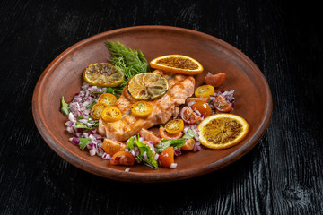 Grilled salmon and vegetables. Laid on a beautiful clay plate, sprinkled with onions, dill and tomatoes.