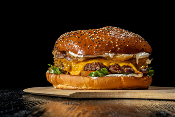 Hamburger with cheddar cheese and onion rings. Beautiful light, black deep background. Beauti big burger.