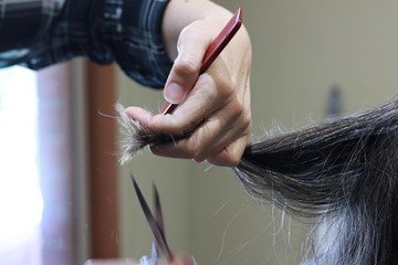 skilled Hands of a hairdresser cutting the curly wavy hair of a customer with hand scissors and a comb