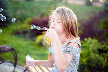 beautiful little girl, teenager, sitting on the bench, blows bubbles. Outdoors