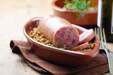Italian large pork sausage cotechino served  with lentils with rosemary on a  rustic plate.