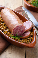 Italian large pork sausage cotechino served  with lentils with rosemary on a  rustic plate.