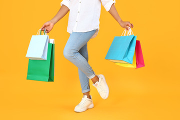 Beautiful African-American woman with shopping bags on color background