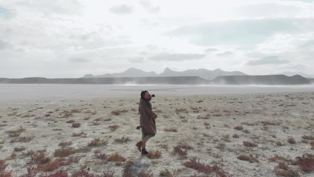 A girl in a coat with a camera walks on a dry salt lake