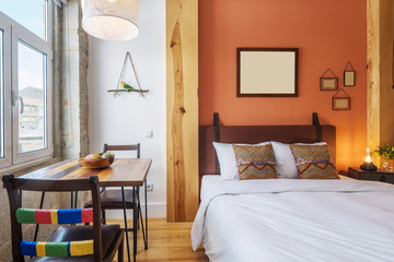 Light modern interior design, studio apartment with double bed, big windows and wooden decor. Orange and white color wall