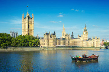 Scenic morning view of the London skyline featuring a boat on the River Thames in front of the Palace of Westminster on a bright summer day
