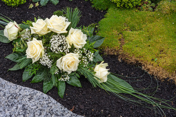 Rosenbouquet mir weißen Rosen auf Erde liegend neben Granitplatte und Moos