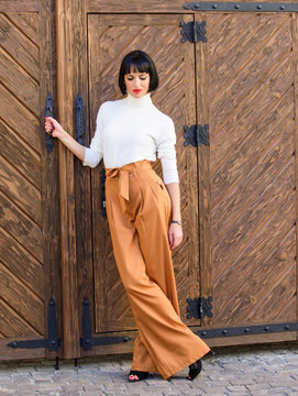 Fashion And Style Concept. Girl With Makeup Posing In Fashionable Clothes. Fashionable Outfit Slim Tall Lady. Woman Walk In Loose Pants. Woman Fashionable Brunette Stand Outdoors Wooden Background