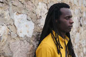 Portrait of  African man wearing long dreadlocks and yellow shirt. Stones wall on background