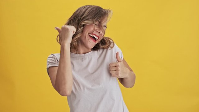 Charming and happy young woman with red lips laughing and dancing over yellow background isolated                                                                          