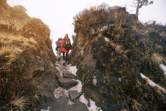 Hikers couple with backpacks walking on top of mountain in fog between two big rocks, Nepal trekking in Annapurna area