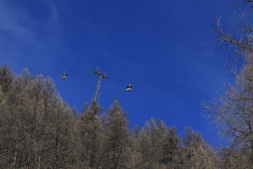 Gondola passing in front of alpine snow mountains and blue sky.