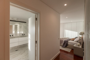 Modern interior design. Bedroom and opened door to White colours Marble bathroom