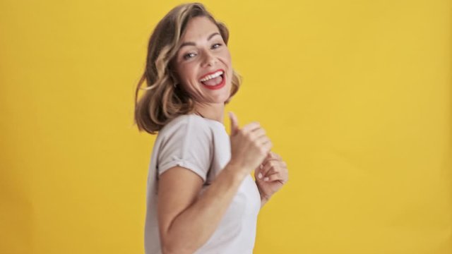 Charming young woman with red lips dancing with arms folded along the body over yellow background isolated                                                                           