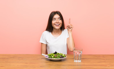 Young woman with a salad intending to realizes the solution while lifting a finger up