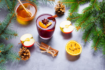 Mulled wine with spices in glass. Red mulled wine with cinnamon, anise and honey. Hot mulled wine at a cement gray background with fir branches and pine cones