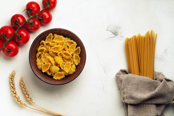 Raw pasta in a plate and long pasta tied in burlap with cherry tomatoes and spikelets of wheat