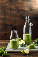 Green smoothie in glass jar and bottle on wooden background