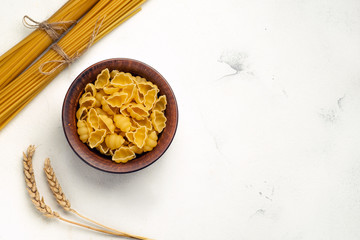 Uncooked pasta in a plate and long pasta tied with a rope with spikelets of wheat and an empty place for text top view