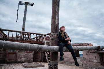A woman pirate sits on a fallen ship's yard. Sea sailboat and a robber girl with a knife in his...