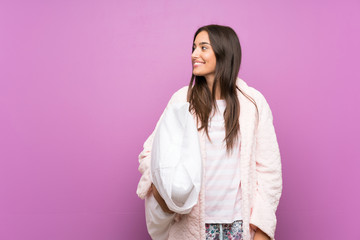 Young woman in pajamas and dressing gown over isolated purple background looking to the side