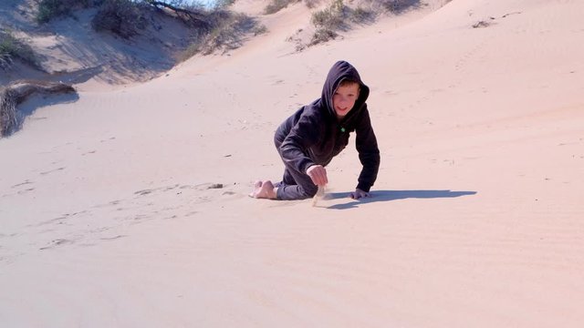 Little boy is playing in sand. Happy child boy crowls and climbs up on sand dune on sea beach at vacation. Outdoor activity in happy childhood.