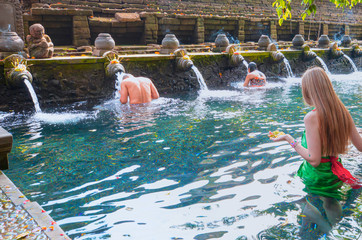 Young girl is praying in holy spring water of sacred pool - Pura Tirtha Empul Temple, Indonesia