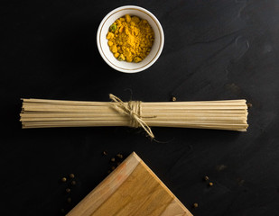 soba - buckwheat noodles (raw buckwheat noodles). Pasta tied with string with seasoning in a Cup on a wooden cutting Board on a dark background.