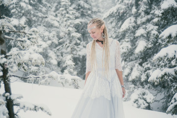 Fototapeta na wymiar Woman wearing elf ears, dreadlocks and white dress in winter snowy Christmas tree forest. Fog and mystery frozen day