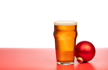 Pint glass of ale or beer with christmas bauble on red background
