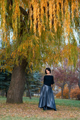 Beautiful elegant woman standing and posing near big yellow tree in a city park in autumn