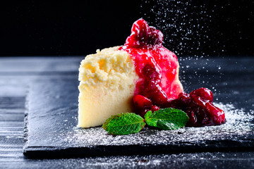cherry cheesecake on a black background with reflection and flying icing sugar - obrazy, fototapety, plakaty