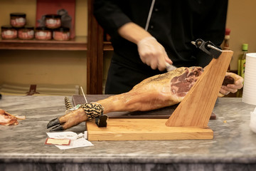 Male hands of seller cutting slices from whole leg of jamon in meat store, in the supermarket