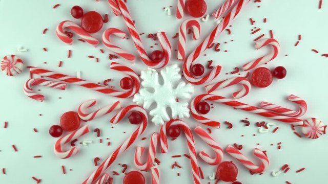 Traditional Christmas day, red snowflake made of peppermint candy cane rotating or spinning seamless in the loop. Slow motion of cinnamon lollipop sweets and sprinkles arranged kaleidoscope.