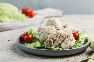 Chicken meatballs in a flat plate with lettuce and cherry tomatoes on a light background