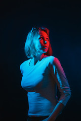 The neon lights of the club. Portrait of a young woman posing in half turn.Side blue and red light. Black background. Vertical